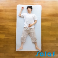 一名男性穿著白色T恤與淺卡其色短褲，仰臥在白色單人睡墊上，睡墊置於木紋地板上。