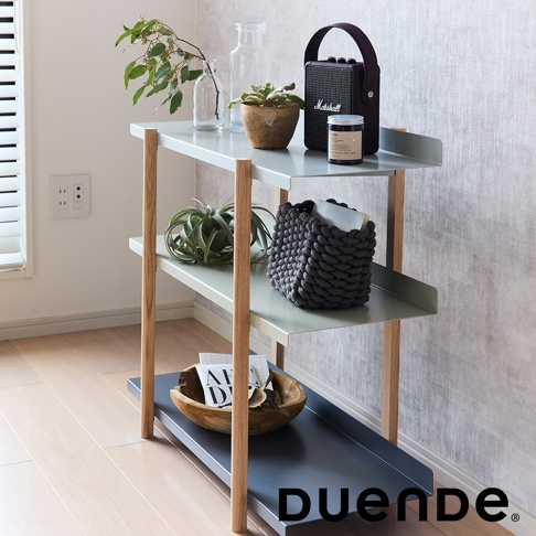 MARGE SHELF 3 三層置物收納架，淺灰綠色金屬層板搭配原木色木質支架，最底層為深灰色金屬盤。收納架上擺放著綠植、音響、罐子、編織籃與木碗，整體設計簡約現代。