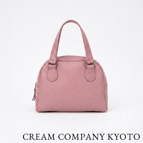 這款由 CREAM COMPANY KYOTO 出品的粉紅色半月形手提包，選用輕量且具耐水性的手感牛皮製成，外型簡約優雅。包身呈現柔和的霧面質感，設有穩固的提把與金屬拉鍊，底部寬敞且容量實用，適合各式日常穿搭。