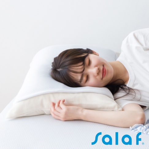 一名女性頭部舒適地枕在白色與米色雙層枕頭上，臉部朝右，閉眼微笑。枕套為白色，表面有細緻的織紋。