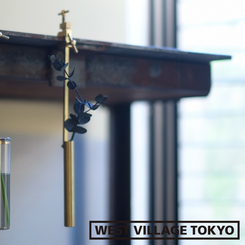 黃銅可夾式金屬花器，細長圓管狀，夾在木質層架上，內插有深色葉片植物。