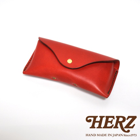 一個紅色的手工皮革眼鏡收納盒，上面有一個金色按鈕。