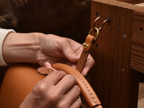 職人手作皮革吊掛扣帶，淺棕色皮革，搭配黃銅色金屬扣環，固定於木質結構上。