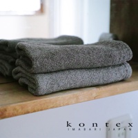 兩條深灰色針織紋純棉毛巾堆疊在木架上，左側有毛巾的鏡面反射。