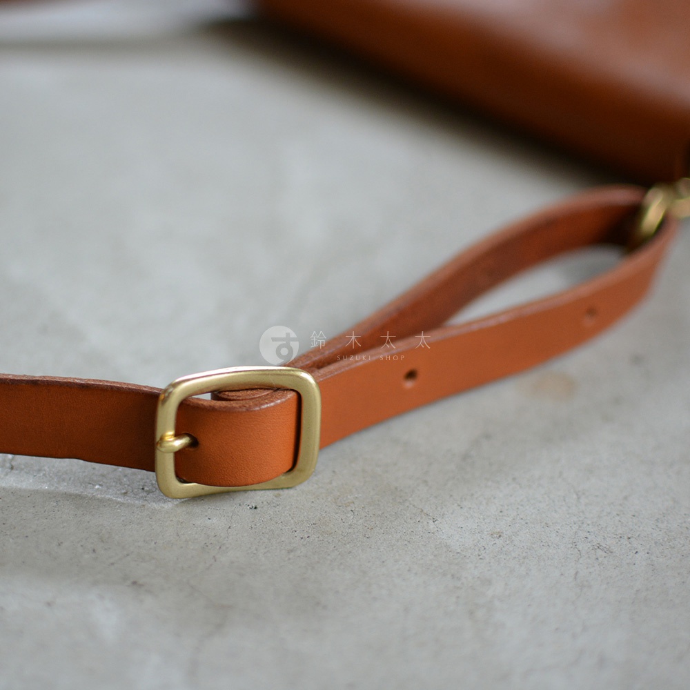 職人手作皮革隨身斜背包，展示細節為焦糖色皮革肩帶與復古黃銅調節環。