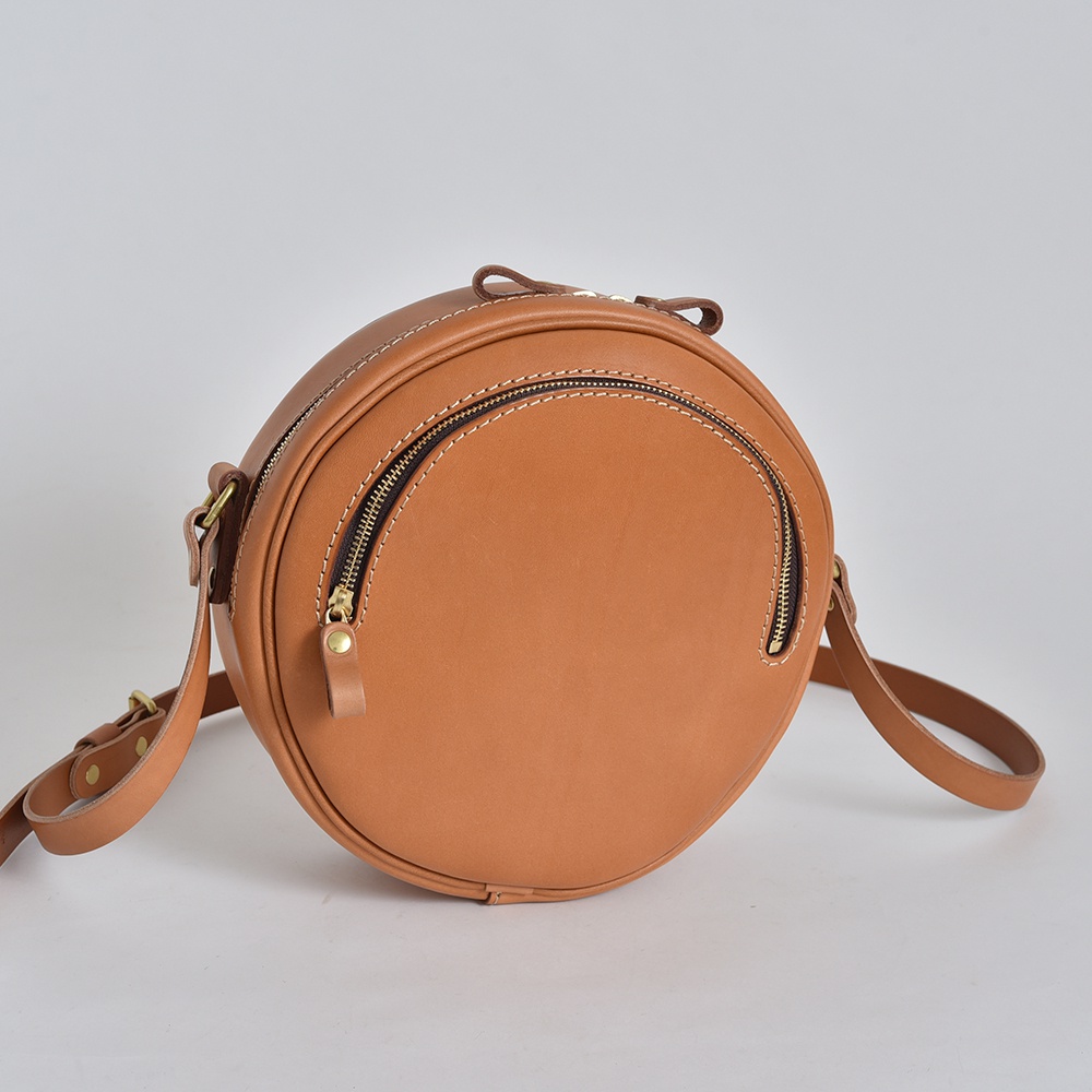 職人手作皮革小圓包，經典圓潤造型，採用棕褐色皮革，配有黃銅色拉鍊和可調節肩帶。