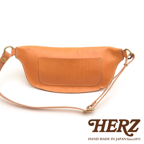 職人手作皮革輕便斜背包，採用棕色天然皮革製作，設計簡約，正面有一個方形皮質插袋，搭配可調節的細皮革背帶與金屬扣環。