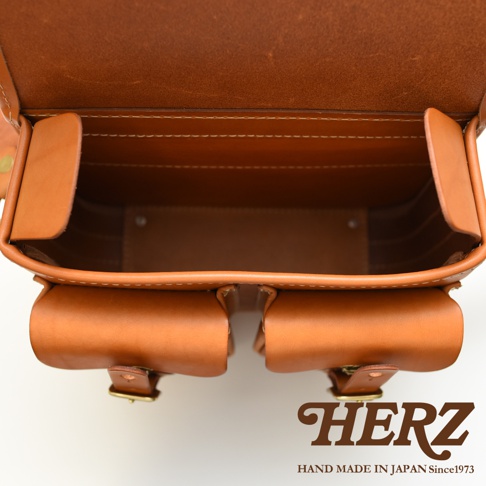 日本HERZ手工皮革經典雙扣郵差包，特寫內部空間與金屬扣細節，品牌Logo印於右下角。