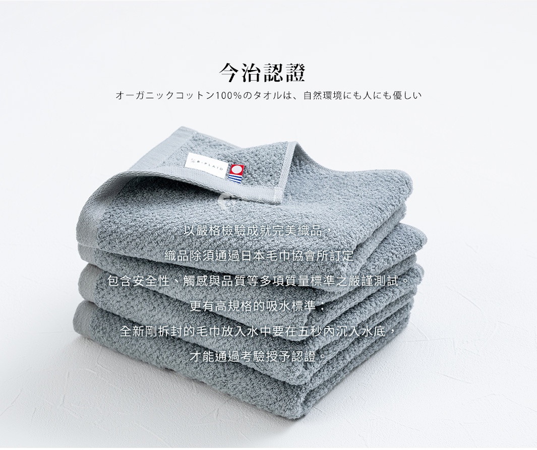 一疊灰色、以鱗紋織法呈現的毛巾，頂部毛巾上有一個標籤，標示「OR-PLAID」字樣及藍白紅條紋。