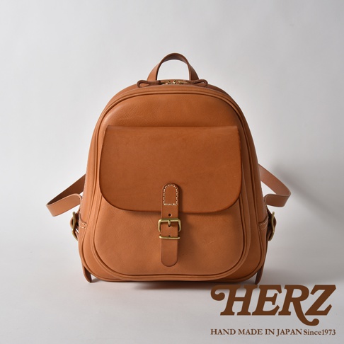 棕色皮革製迷你後背包，正面有立體口袋，以金屬釦帶固定，肩帶與包身相連。