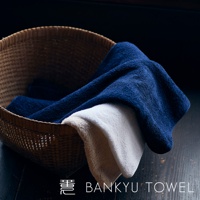 編織籃中疊放著三條毛巾，深藍色、白色和淺褐色。毛巾材質柔軟，紋理清晰可見。