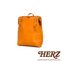 橙色皮革後背包，款式為職人手作，設計有金屬扣環與皮革束帶，簡約大方。