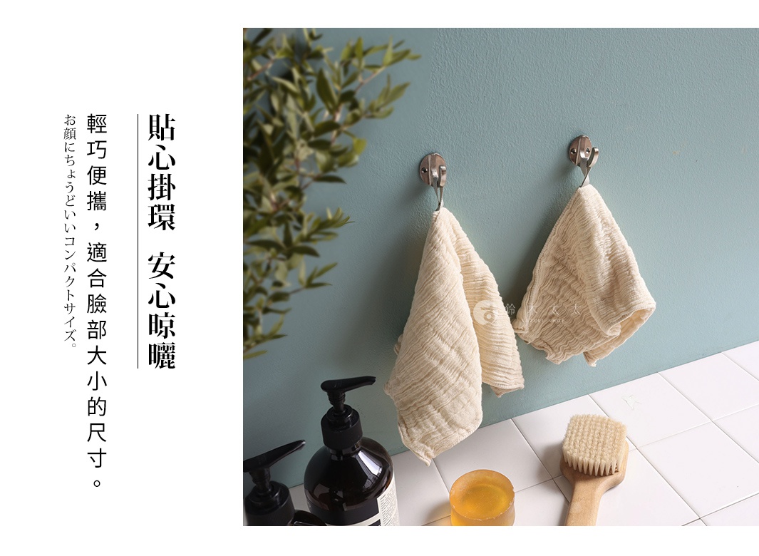 兩條米白色立體褶皺紗布洗臉巾掛在淺藍色牆壁的掛鉤上，旁邊有綠葉植物點綴，下方擺放著兩個黑色壓頭瓶裝的沐浴乳，以及一塊圓形黃色皂和一個木質刷頭的沐浴刷。