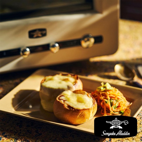 千石阿拉丁烤箱旁擺放著兩個烤麵包盅，裡面填滿了融化的起司，旁邊還有一份色彩繽紛的絲狀沙拉。