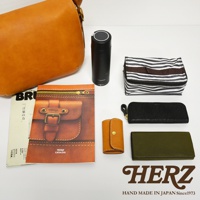 職人手作皮革復古翻蓋郵差包，搭配黑色保溫瓶、黑白條紋收納包、黑色長夾、橘色鑰匙包和墨綠色長夾。