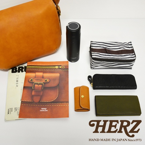 職人手作皮革復古翻蓋郵差包，搭配黑色保溫瓶、黑白條紋收納包、黑色長夾、橘色鑰匙包和墨綠色長夾。