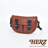 職人手作皮革傳統釣魚包，採用棕色皮革，配有黑色皮質翻蓋、雙皮帶扣和金色金屬扣。包身呈現半月形，帶有肩帶。