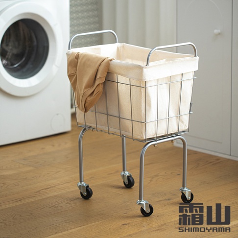 鐵藝復古風移動式洗衣籃，配有四個萬向輪，籃身為銀色金屬網格，內襯為米白色帆布，籃子上方掛有一件棕褐色衣物，整體呈現簡約實用的風格。