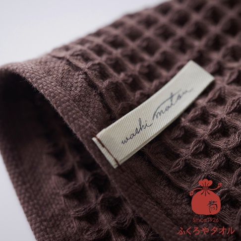 深棕色格子紋理毛巾，帶有白色標籤，上面印有 washi matsu 字樣