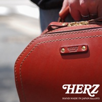 酒紅色皮革立體商務後背包，展現細緻手縫線條與黃銅五金細節，左側有品牌標誌銘牌，右下角為品牌Logo與「HAND MADE IN JAPAN Since1973」字樣。