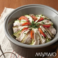 深灰色陶土鍋內盛裝著一道由雞肉片、櫛瓜片和番茄片堆疊而成的料理，表面撒有香草碎。