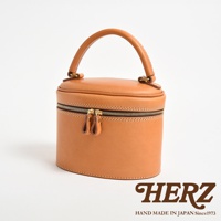 職人手作皮革圓筒型化妝手提包，以天然植鞣皮革製成，呈現溫潤的淺棕色。包款設有雙拉鍊開口，配有皮革拉環，頂部有圓弧形提把，整體造型簡潔且實用。