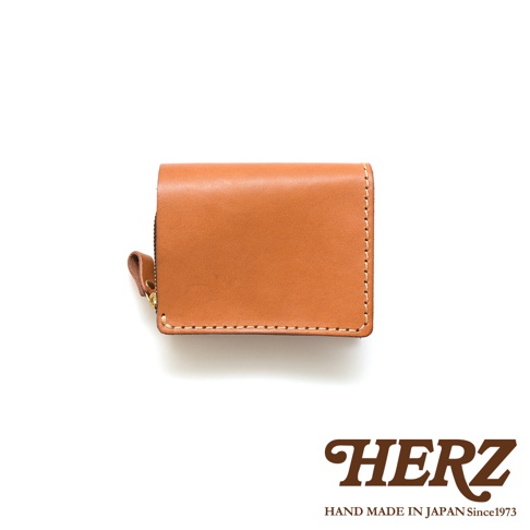 一個駝色皮革製成的小型雙折短夾，附有拉鍊開合及皮革拉片，邊緣有縫線裝飾。