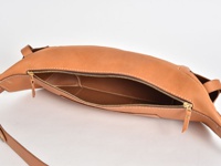 淺棕色皮革斜背包，拉鍊敞開，露出內裡隔層。包身線條圓潤，搭配金色拉鍊和細緻縫線，整體呈現質感。