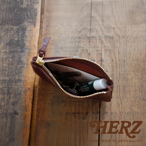 職人手作咖啡色皮革拉鍊式小物收納袋，內含多把鑰匙與護唇膏，袋口以金色拉鍊開合，皮革質感紋理清晰。