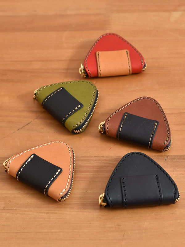 五個三角形皮革零錢包，外觀設計成飯糰造型。顏色包含紅、綠、棕、褐和黑色，皆配有黑色或淺棕色皮片裝飾，並以白色縫線勾勒邊緣，搭配金色拉鍊。