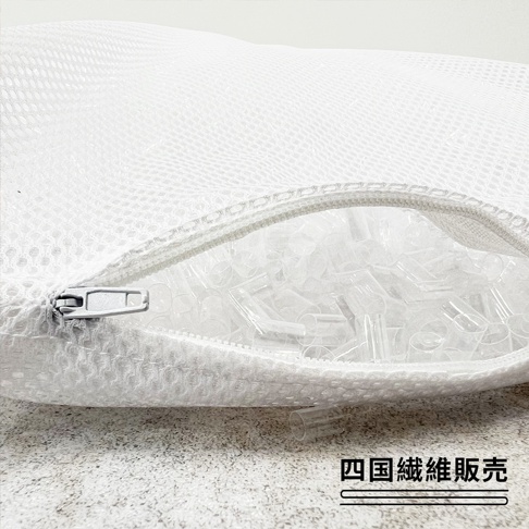 一個裝有透明塑料軟管枕芯的白色網狀收納袋，拉鍊處呈現半開狀態露出內部細節，右下角標註有四國纖維販賣字樣，整體呈現簡約實用的居家收納風格。