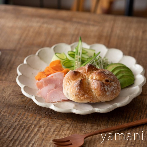 一個帶有花瓣邊緣的白色陶瓷盤，盛有麵包、火腿片、胡蘿蔔絲、小黃瓜片、豆芽和酪梨片。