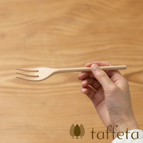 一只手正拿著一個淺色楓木製成的三齒餐叉，餐叉的背景是木紋桌面。