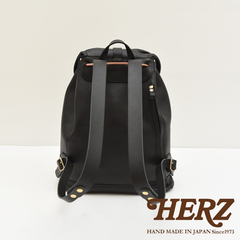 職人手作黑色皮革單扣束口後背包 R-5，背面視角。包身採用柔軟皮革，配有兩條寬版皮革肩帶，肩帶底部及側邊有金屬扣環及鉚釘裝飾。