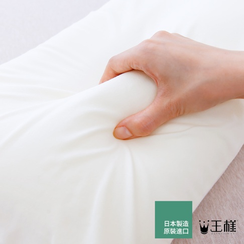 白色乳膠枕，表面柔軟，手感可塑性強，呈現細緻的紋理，左下方有綠色日文標籤和「王樣」品牌標誌。