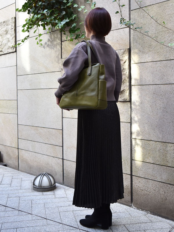 橄欖綠皮革直式肩背托特包，側面有口袋設計，搭配灰色針織上衣和黑色百褶長裙。