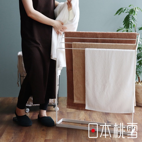 白色金屬毛巾架上掛有多條飯店方巾，顏色包含深棕色、淺棕色和白色。方巾材質看起來柔軟吸水，適合居家或飯店使用。