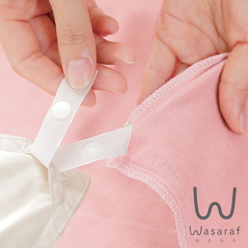 雙手正在操作一件粉色雙層紗材質的被套，被套邊緣有縫線，並附有白色織帶及按扣，用於固定。