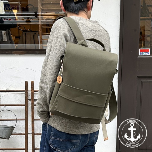 一名男性背著一個軍綠色高島帆布前蓋式背包，背包上有一個小巧的船錨吊飾。