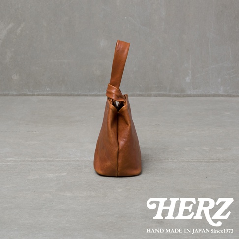 棕色皮革單柄手提包，包身柔軟，提把處有扭轉設計，整體呈現簡約風格。