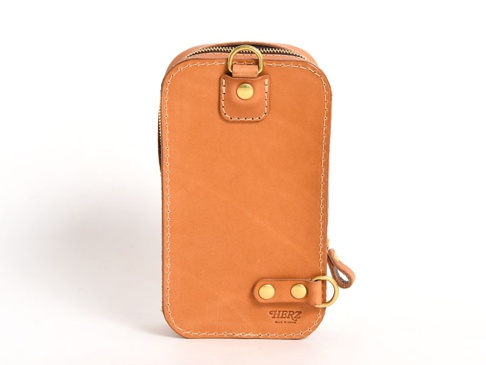 淺棕色皮革製成的直立型斜背包，頂部有拉鍊開口，側面有 D 型環和固定帶，底部有品牌標誌。