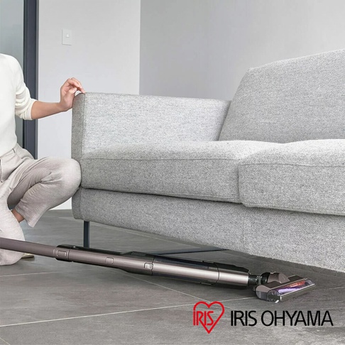 灰白色布藝沙發旁，灰色充電式吸塵器正在清潔地板。