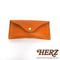 手工製作的橘棕色皮革眼鏡套，配有金色摁扣，邊緣縫線清晰可見，下方印有HERZ品牌標誌。