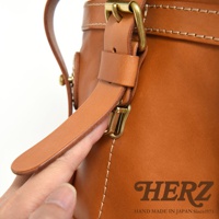 職人手作的棕色皮革後背包，特寫其皮質肩帶、黃銅扣環和縫線細節。