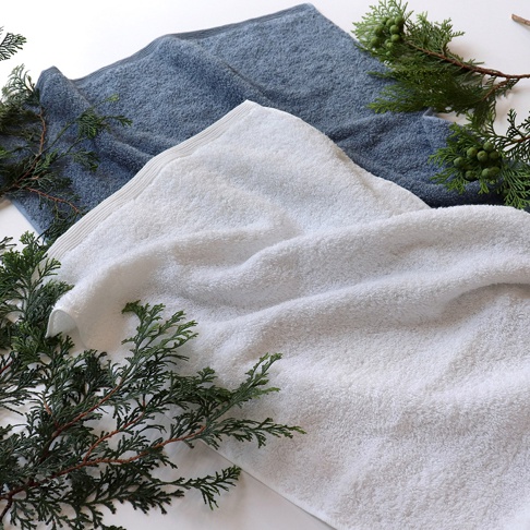 兩條精梳棉迷你浴巾，一條為純白色，另一條為淺灰色，皆有檜木綠葉裝飾。
