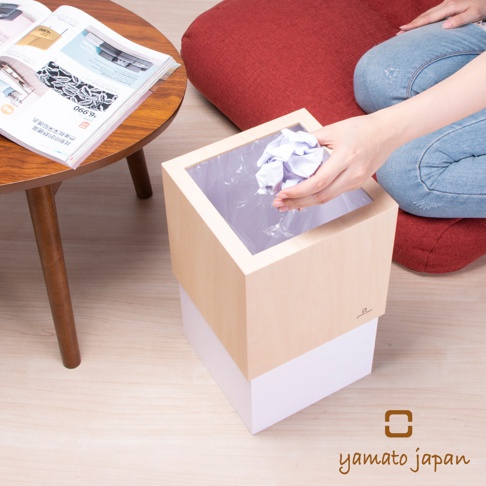 淺木紋色與白色搭配的方形積木垃圾桶，內部有透明塑膠袋，一只手正將揉成團的紙張丟入。