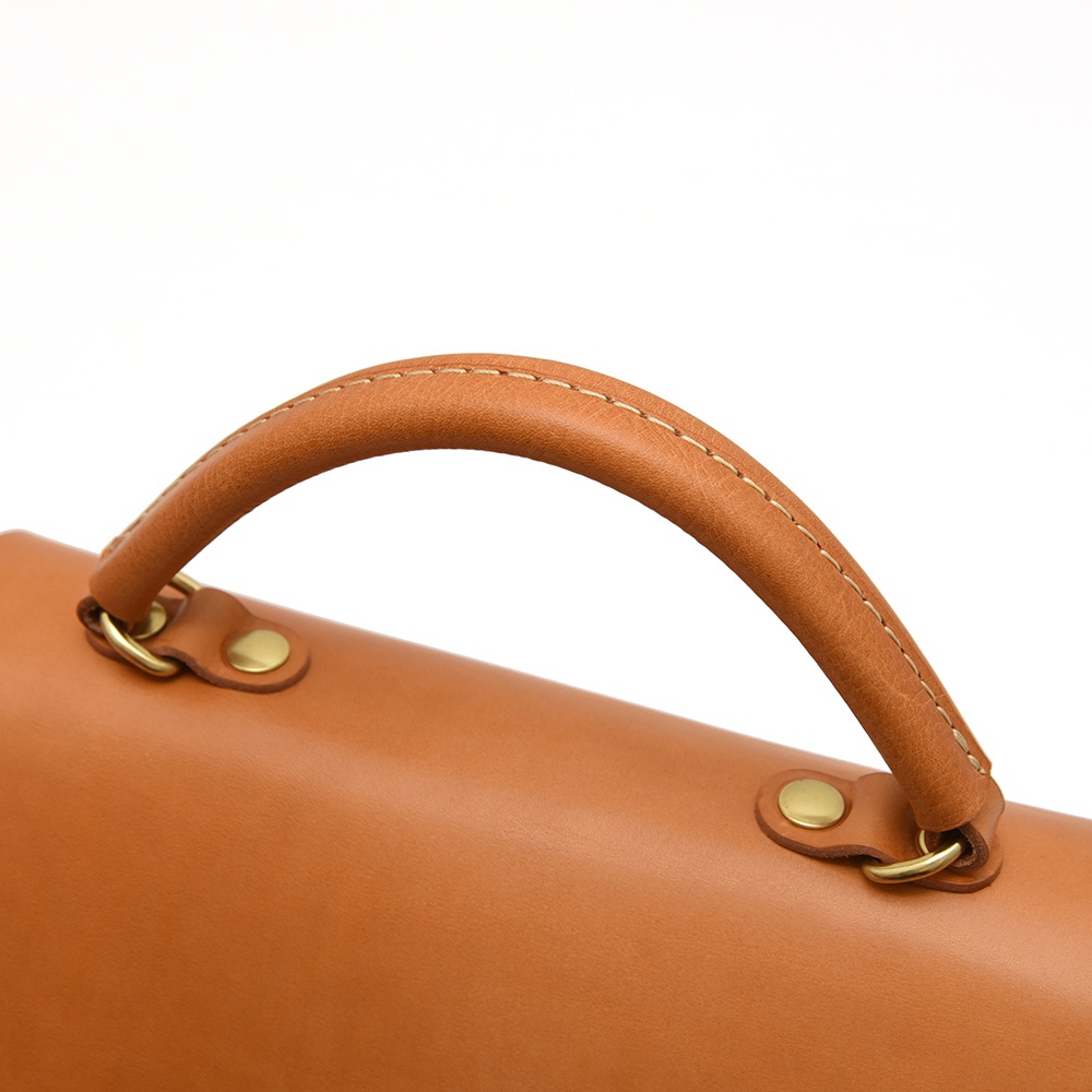 HERZ 職人手作皮革包的棕色皮革提把，帶有縫線細節，並透過金屬卯釘連接至包身。