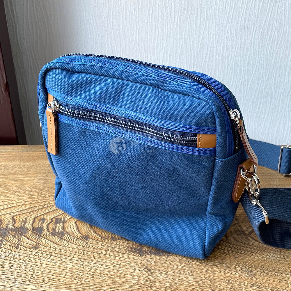 深藍色石洗帆布散步包，有兩個拉鍊前袋，配有棕色皮革拉頭，背包帶為深藍色。