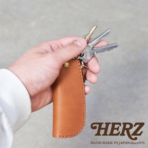 手持一只棕色皮革鑰匙包，內有數把金屬鑰匙。皮革鑰匙包有精細的縫線和一個黃銅卯釘。