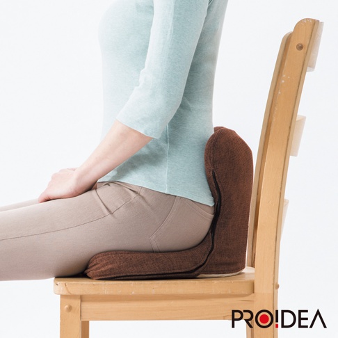 馬鞍型正姿座墊，咖啡色織紋布料，中間有拉鍊設計，支撐腰部與臀部，放在木質椅子上。